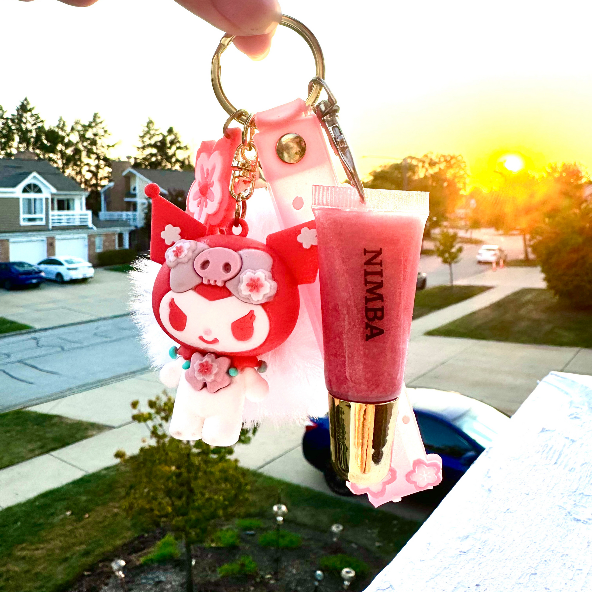 NIMBA pink lip butter keychain against a sunset backdrop, paired with cherry blossom-themed charms for a vegan, natural beauty gift