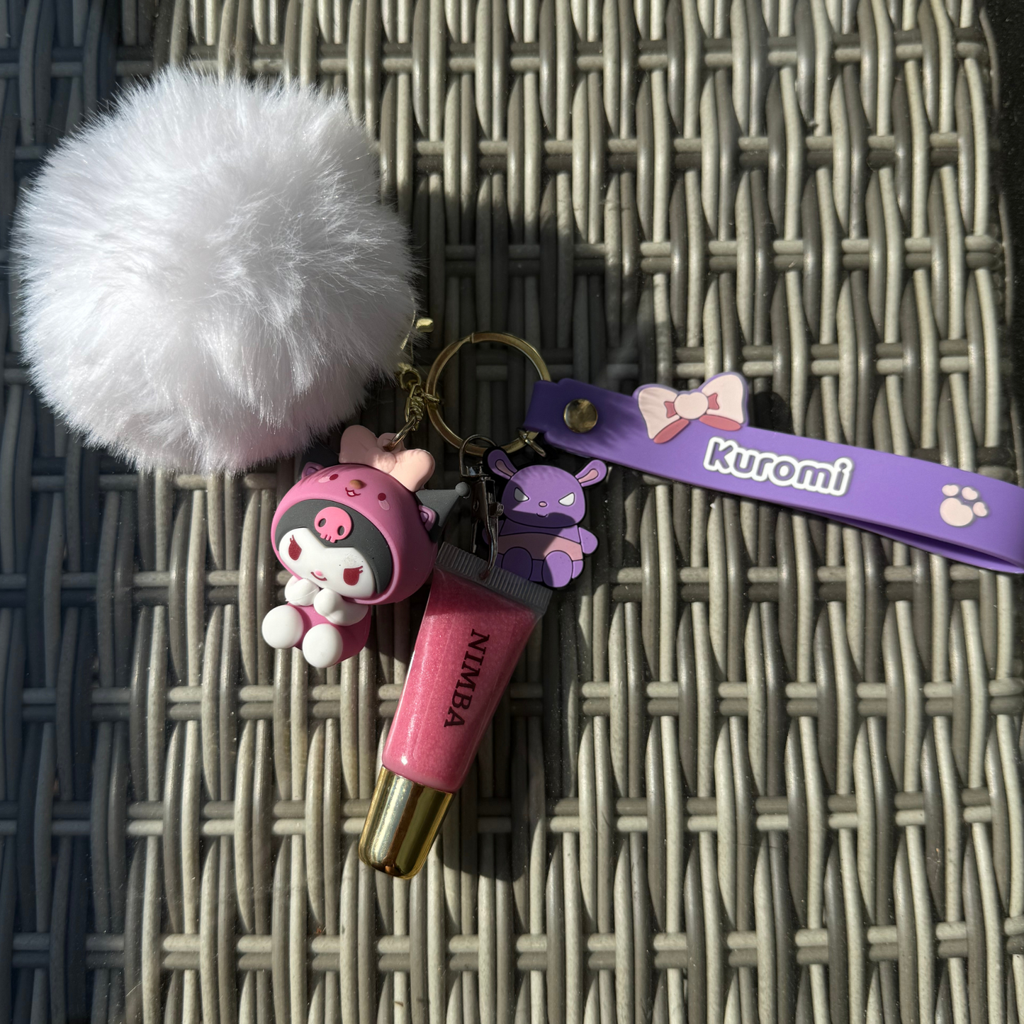 NIMBA lip gloss with a Kuromi-themed keychain featuring a purple strap, bunny charm, and fluffy white pom-pom. A stylish and practical beauty accessory