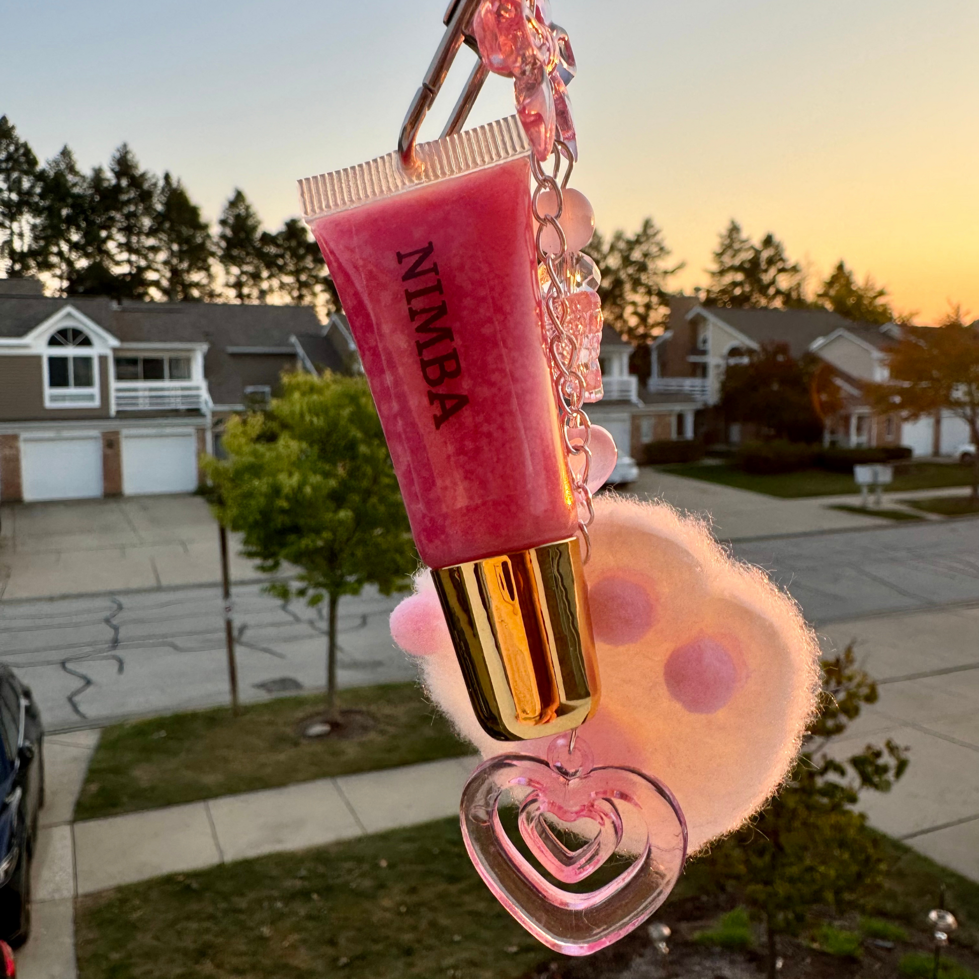 NIMBA lip gloss in pink, featured with a fluffy white charm and cherry blossom keychain. A vegan, moisturizing, and travel-friendly lip care solution